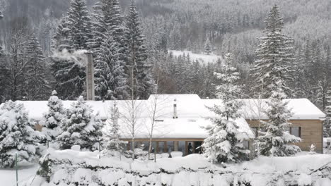 Casa-Moderna-Con-Una-Chimenea-Humeante-En-Un-Bosque-De-Invierno,-Nieve,-Chequia