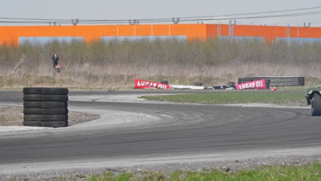 Toma-En-Cámara-Lenta-De-Un-Coche-Verde-A-La-Deriva-En-Una-Pista-De-Carreras-Con-Un-Montón-De-Neumáticos-Y-Giro-S