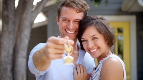 portrait of happy couple standing outside new home with keys