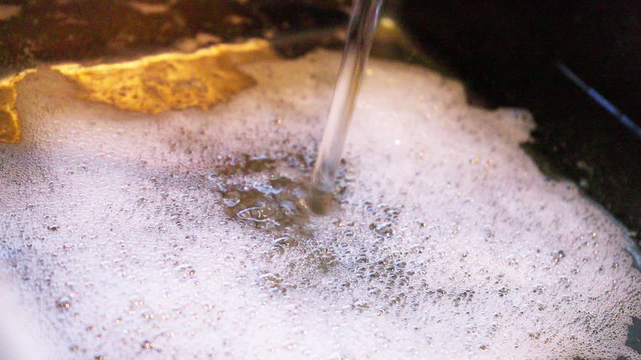 Water and soap create thick foam in kitchen sink washing up or dishwashing, home