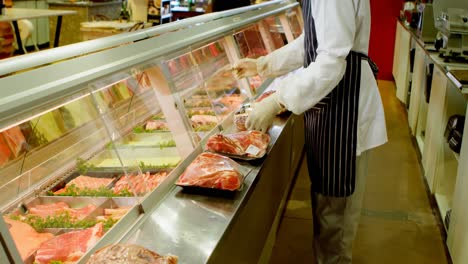 carnicero organizando carne envuelta en el refrigerador en la tienda 4k