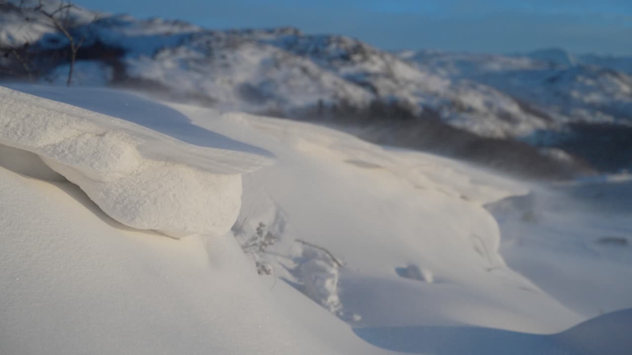 Macro closeup view of snow drifting blown across pile with mountains behind