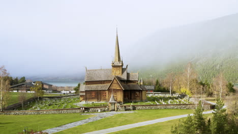 Wooden-Exterior-Facade-Of-Lom-Stave-Church-Against-Misty-Forest-Mountains-In-Lom,-Norway