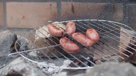 primer plano de una persona irreconocible volteando salchichas a la parrilla con lenguas de metal