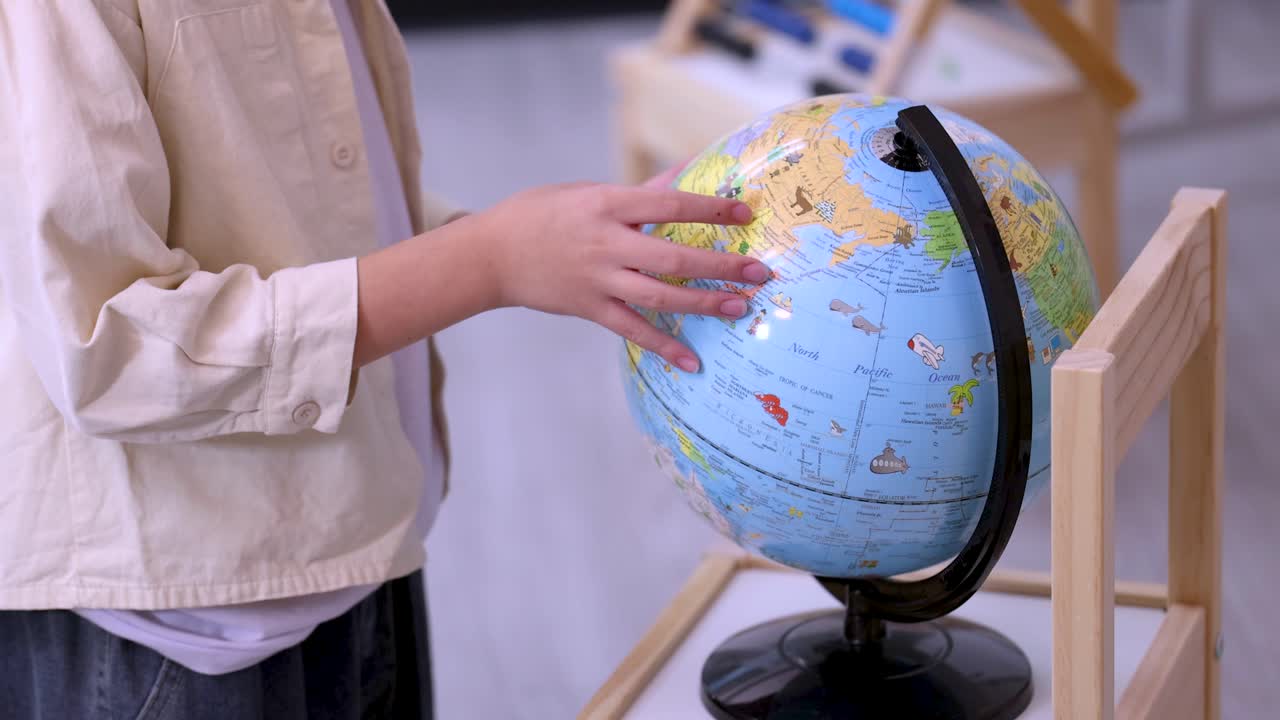 Young student spins and touches educational world globe in bright classroom, shallow focus shot
