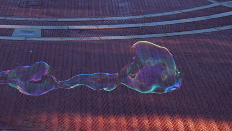 forma de burbuja de jabón flotando sobre el suelo expandiéndose y estallando, arrastrada por la brisa a baja altura, explosión de forma transparente colorida