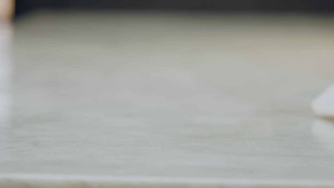 Close-up of a chef's hands placing a green apple, a peeler, and a knife next to a white chopping board on a white countertop