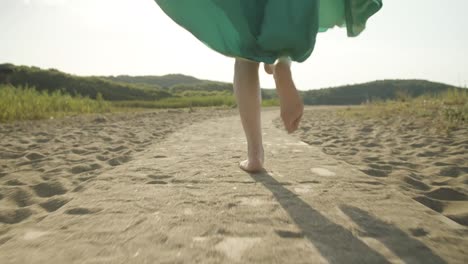 low angle view of women running barefoot along sandy path with fluttering green dress against warm sunshine light