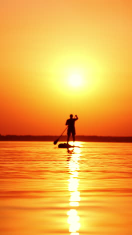 beautiful sunset over the river. man on a sup board approaching camera. low angle view. vertical video