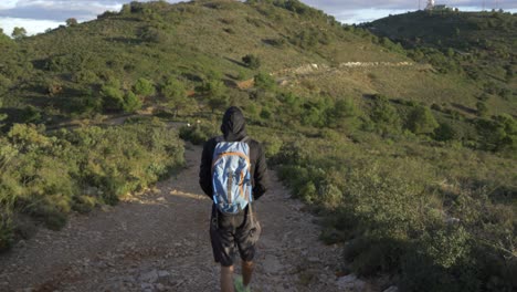 Hombre-En-La-Cima-De-Una-Montaña-Caminando-Por-La-Montaña-Al-Amanecer-Con-Una-Sudadera-Con-Capucha-Negra-Y-Pantalones-Cortos