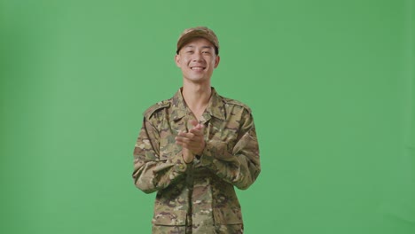 asian man soldier smiling and clapping his hands while standing in the green screen background studio