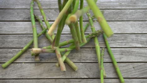 Zeitlupenaufnahmen-Von-Einem-Bündel-Frischer,-Grüner-Spargel,-Die-Auf-Einen-Holztisch-Fallen