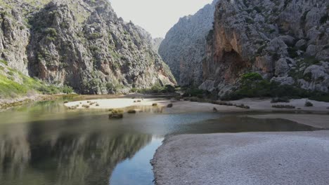 Scenic-drone-view-of-a-valley-at-sa-calobra-Mallorca-with-water-running-beneath-and-mountains-towering-on-the-sides