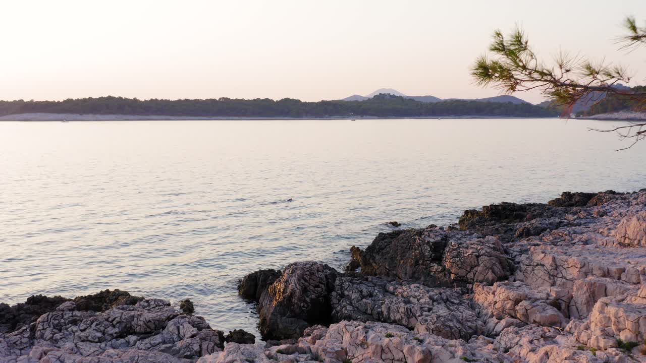 Relaxing snorkling on calm water next to purply rocky shore on sunset