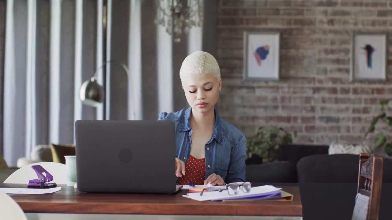 Busy biracial woman working at home with laptop in slow motion