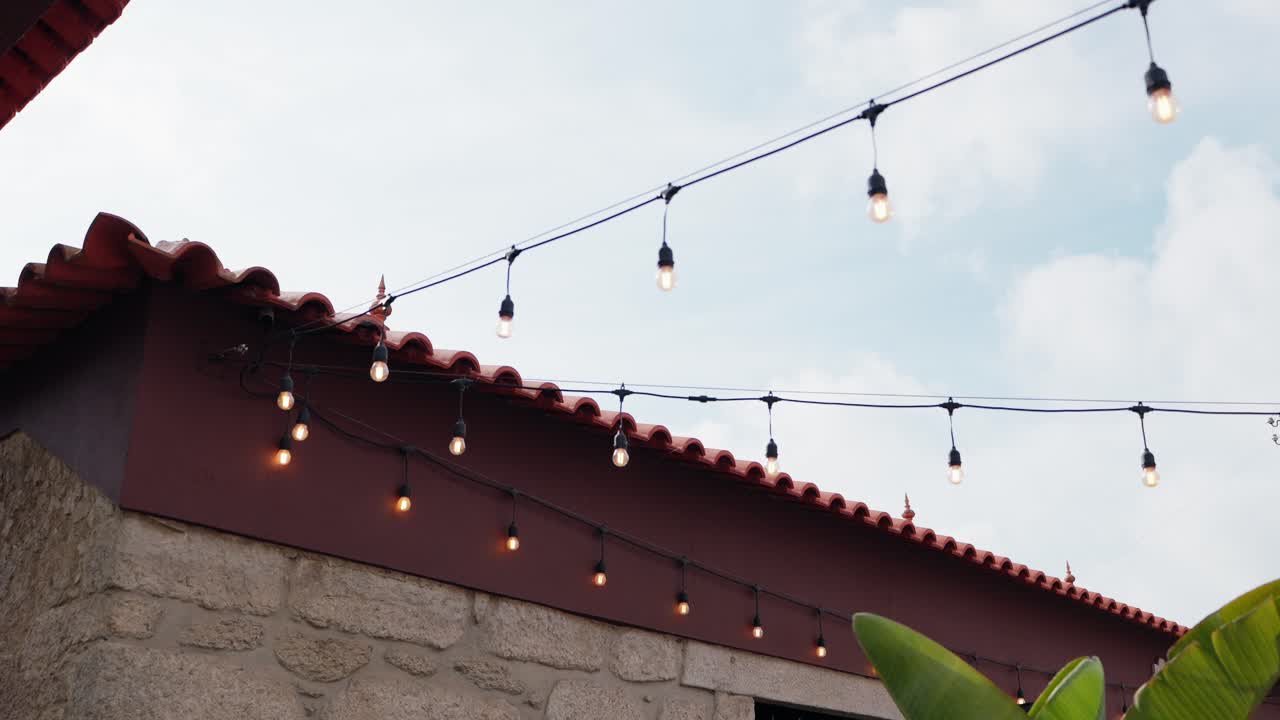warm bulbs hang across terracotta roof of traditional stone building in Portugal evening