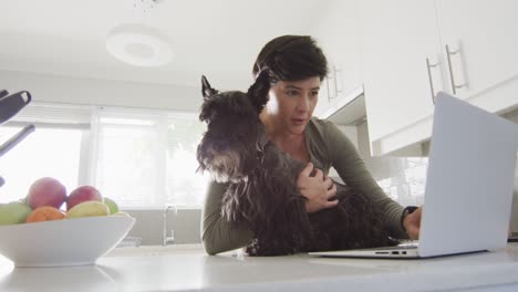 caucasian woman holding her dog and using laptop at home