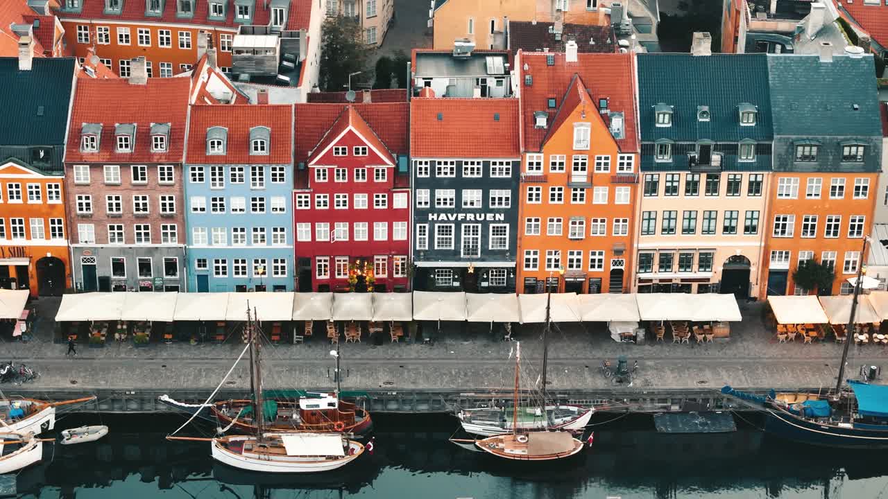 Tracking aerial view of Nyhavn canal at sunrise with boats and glowing buildings in Copenhagen