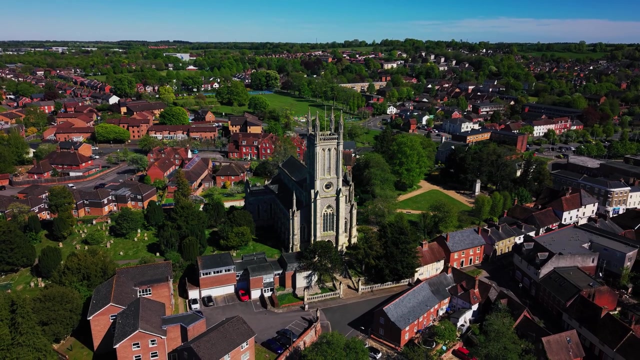 Imágenes aéreas de dron de la Iglesia de St Mary en Andover, mostrando la histórica torre de la iglesia, el cementerio, los tejados circundantes, carreteras, árboles, espacios verdes y el paisaje urbano más amplio de Hampshire en un día soleado