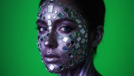 a mesmerizing portrait of a woman with shimmering mirror-like face art, set against a vivid green background, showcasing unique makeup craftsmanship and intricate detail