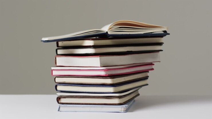 Una pila di vari libri rilegati e in brossura su uno sfondo neutro, con spazio per il testo