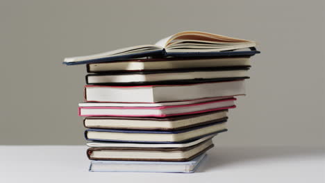 A-stack-of-various-hardcover-and-paperback-books-sits-against-a-neutral-background,-with-copy-space