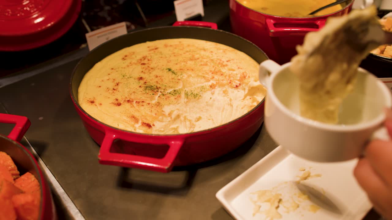 Seseorang menyendok kentang tumbuk lembut dari panci besi cor merah ke dalam mangkuk.