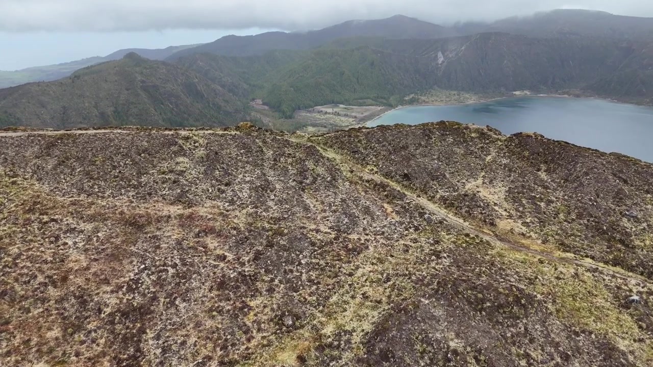 Volo di drone ad alta quota sopra le creste e le montagne aspre che circondano Lagoa do Fogo, Azzorre. Vista aerea panoramica del terreno vulcanico e del lago nascosto sull'isola di São Miguel