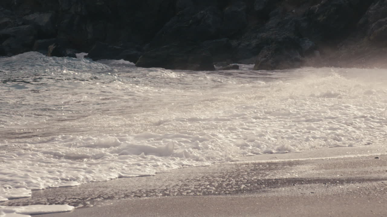 Tracking slow motion shot of a wave breaking onto the shore. The camera pans smoothly with the motion, revealing texture, foam, and steady flow