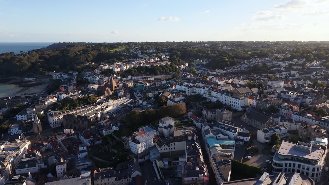 Aerial footage of St Peter Port Guernsey high but detailed flying south in later afternoon sun with sea in the distance