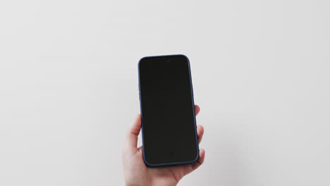 Video-of-caucasian-woman's-hand-holding-smartphone-with-blank-screen-on-white-background