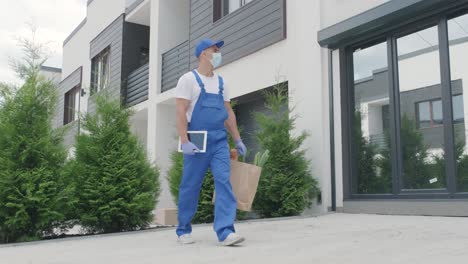 young courier wearing protective mask and gloves deliver a shopping package with food directly to a customer home with safety. food delivery, home delivery in quarantine