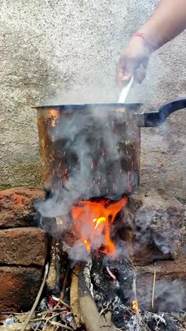 in an open space in maharashtra, india, food is being prepared on a traditional chulha. wood crackles in the fire beneath a metal cooker, as smoke swirls gently in slow motion, evoking rustic charm