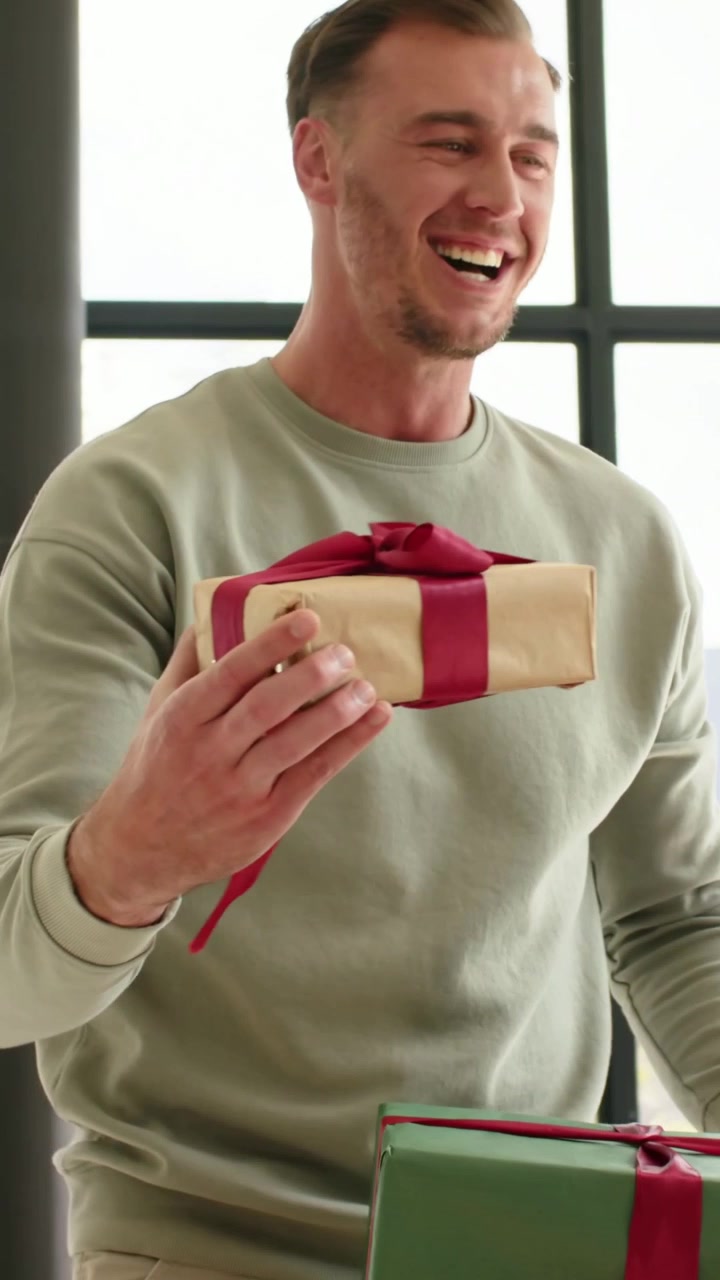 Video verticale: Vedendo un regalo dorato, un uomo che ride con corna verdi consegna un regalo verde da condividere a casa.