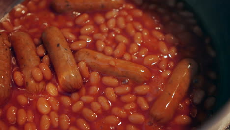 close up of baked beans and sausages cooking in a saucepan