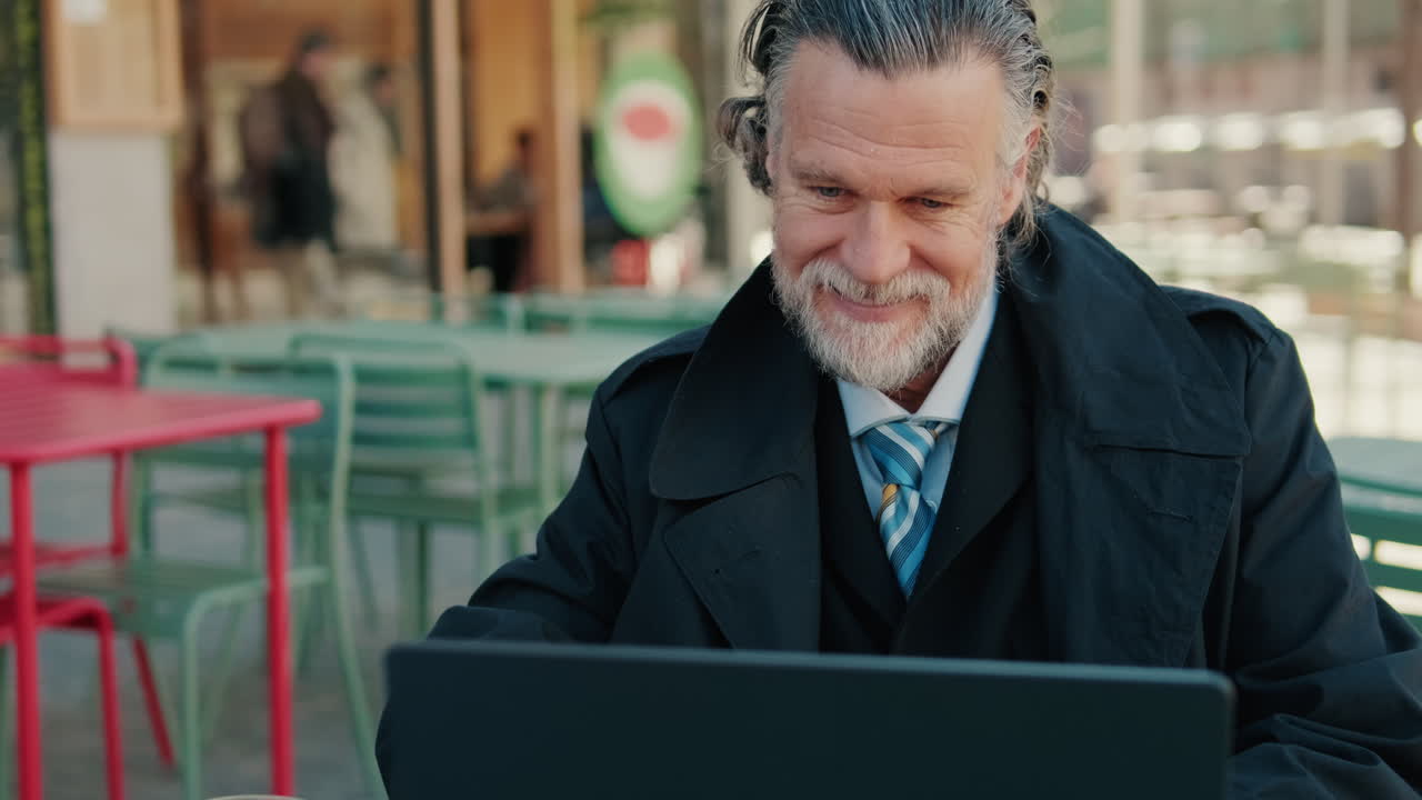 Smiling Senior Businessman Working at Outdoor Cafe