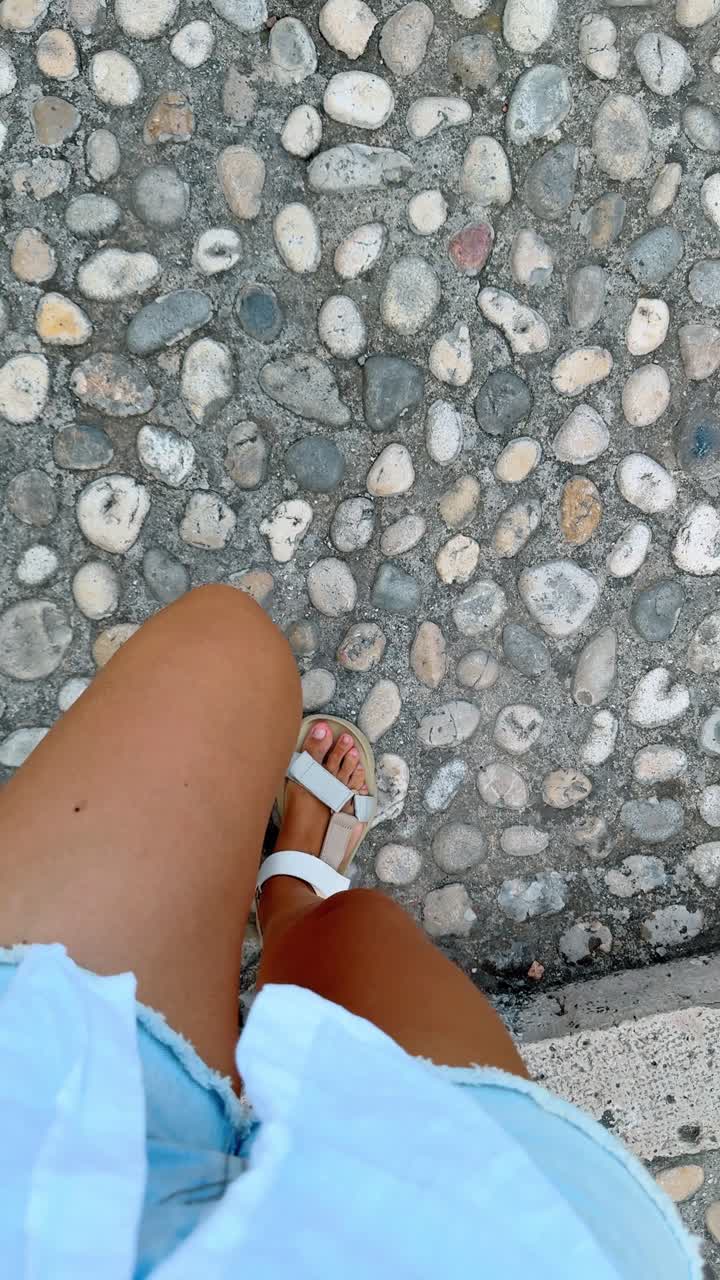 Persona che cammina su una tradizionale pavimentazione in ciottoli in Spagna. Vista dall'alto di gambe con sandali bianchi che camminano su una strada acciottolata e testurizzata in una città spagnola