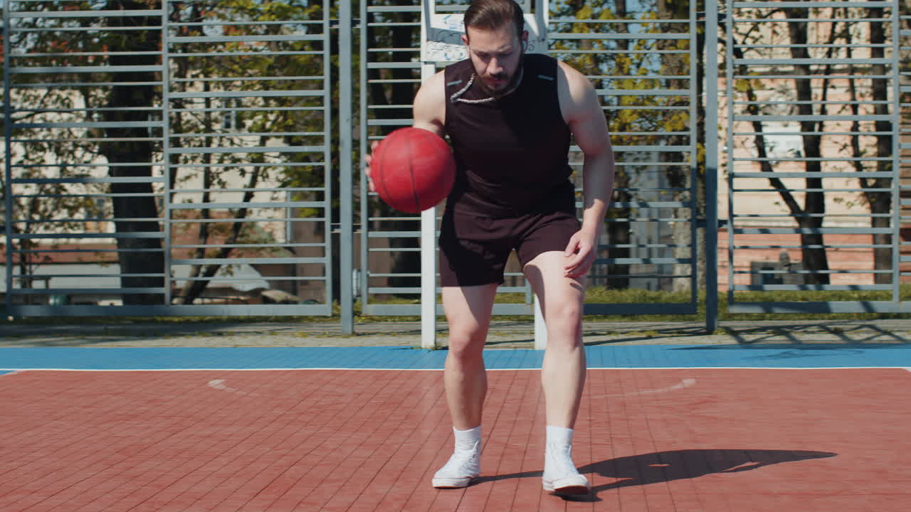 Athletic lebanese man in sportswear playing basketball game dribbling kicks ball on urban city court