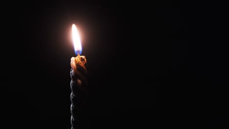 a single candle is lit on a black background. candle flame in the dark