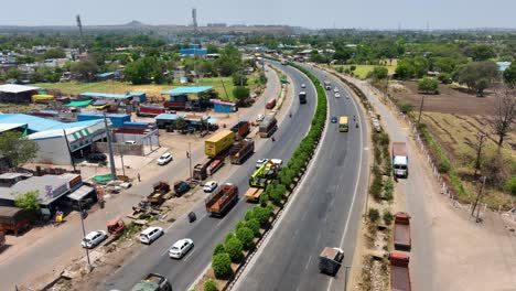 Aerial-shot-of-delivery-trucks-driving-along-a-highway-in-Maharashtra,-india