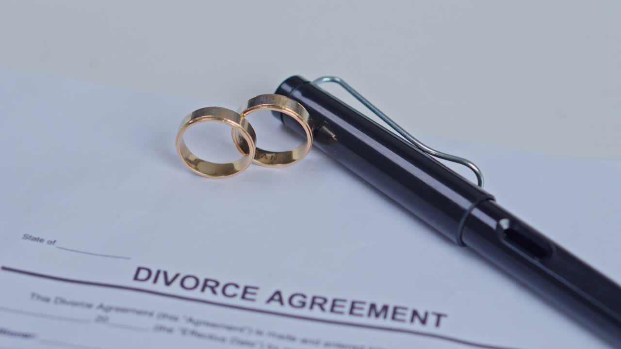Two gold wedding rings and black pen resting on signed divorce agreement paper