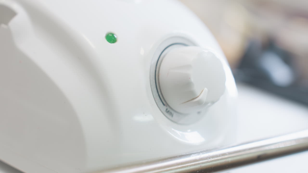 Detailed view of white electric tool showing rounded knob with grip ridges and green indicator light, captured in a clean, bright setting emphasizing surface design and minimalistic aesthetic