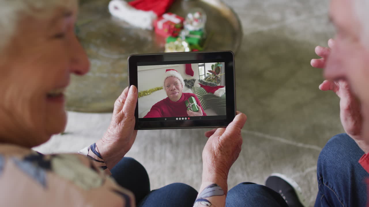 Coppia anziana caucasica utilizza un tablet per una videochiamata di Natale con un uomo felice sullo schermo