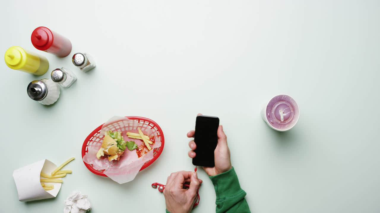 vista superior hombre conectando auriculares a teléfono móvil en un restaurante de comida rápida americano manos desde arriba - dragón épico rojo