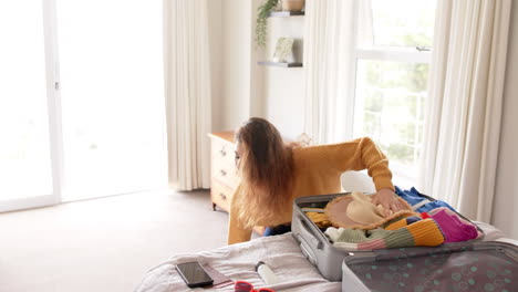 Caucasian-woman-packing-suitcase-on-bed-at-home,-copy-space,-slow-motion