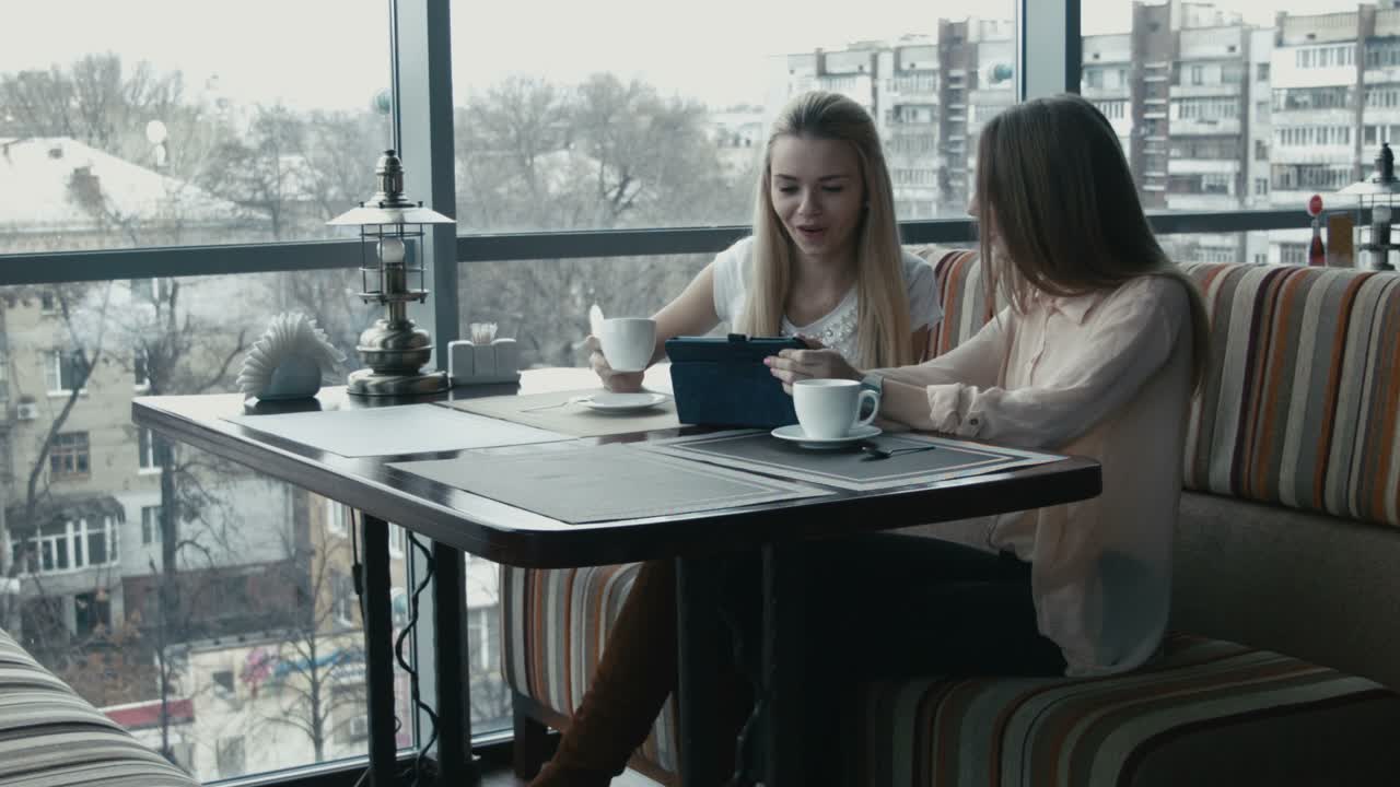 Blonde Girl Showing Photos on Tablet to African Girlfriend. Multicultural Girls Watching Photos o