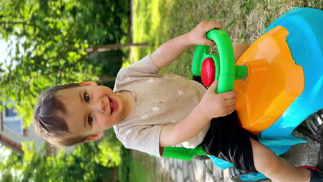 caucasian baby boy riding cheerfully his toy car. joyful time spending outdoors in summer. vertical screen.