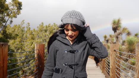 eine hübsche frau, die nach einem regensturm mit einem regenbogen im bewölkten himmel nach zeitlupe des schlechten wetters lächelt und glücklich aussieht