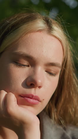 lady in grey clothing sitting under tree with her head resting on her right hand, sunlight softly illuminating her face, she appears deep in thought, eyes slightly closed, as she holds an open book