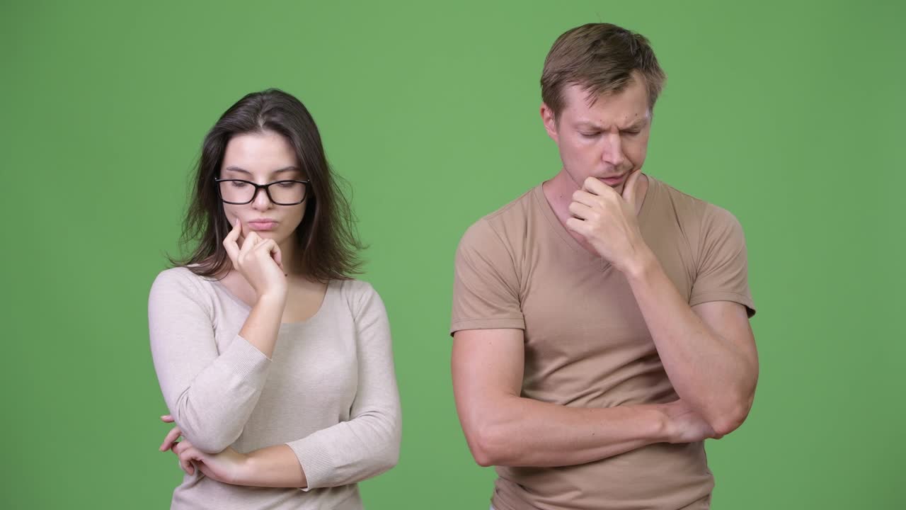 Young sad couple thinking together against green background